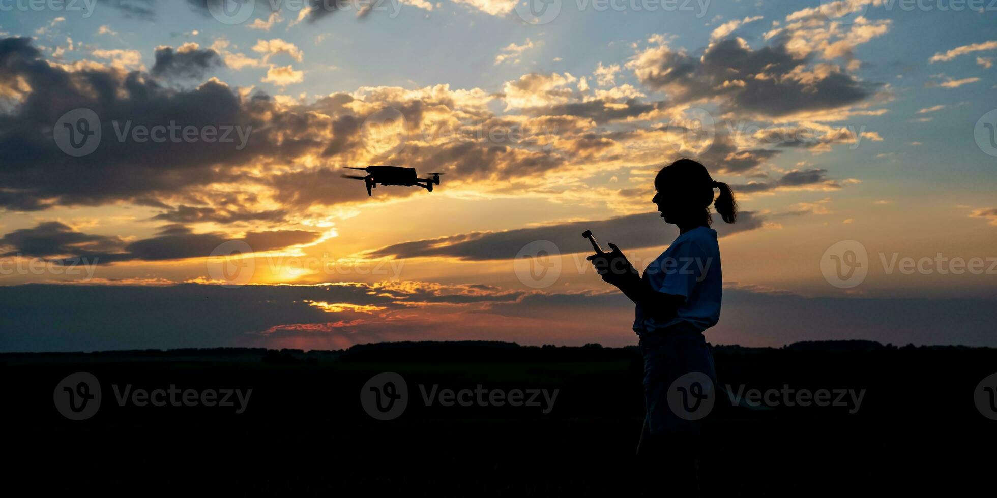 silhouette of woman controlling drone on sunset background photo