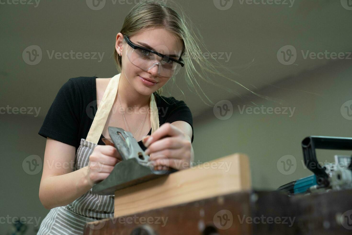 Young beautiful carpenter woman working with wood plank, a female craft worker making wooden furniture in a woodworking workshop. photo