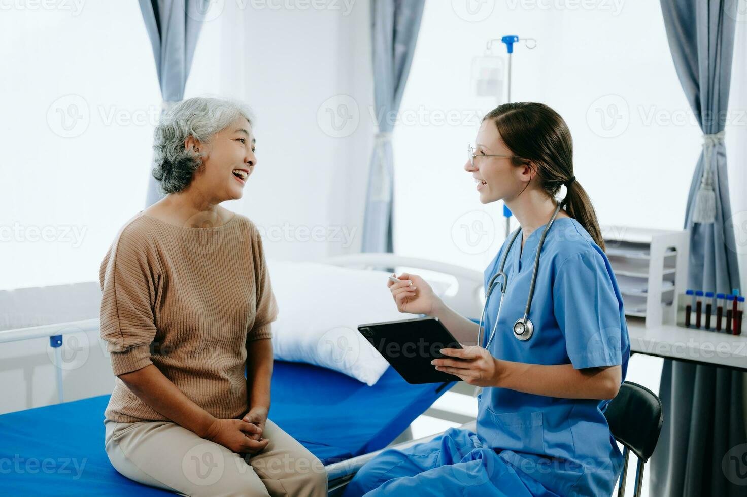 Friendly Female Head Nurse Making Rounds does Checkup on Patient Resting in Bed. She Checks tablet while Man Fully Recovering after Successful Surgery in hospital photo