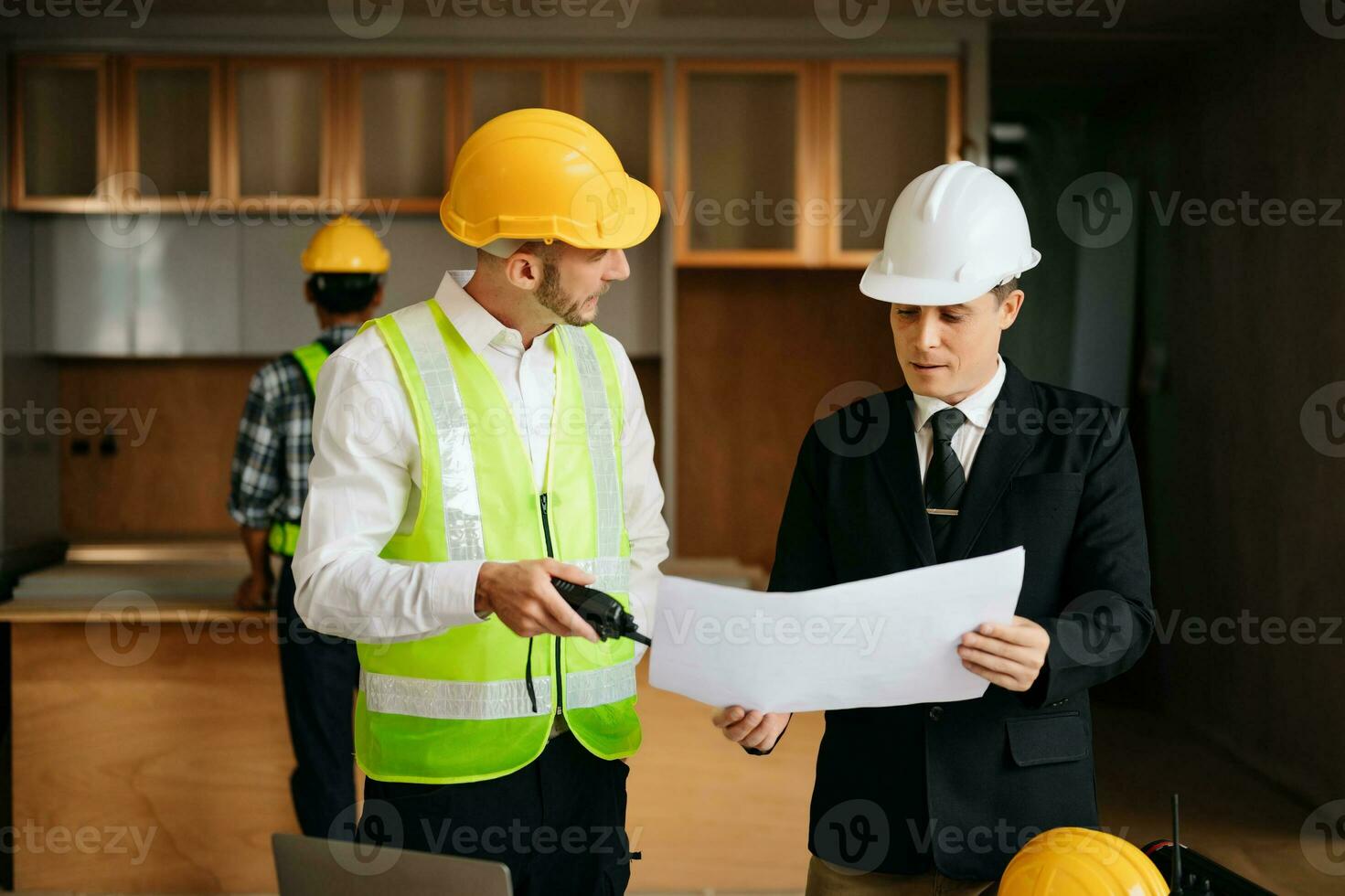 Contractor and architect looking at plan, tablet, laptop and talking about working on big project. Building in construction interior. photo