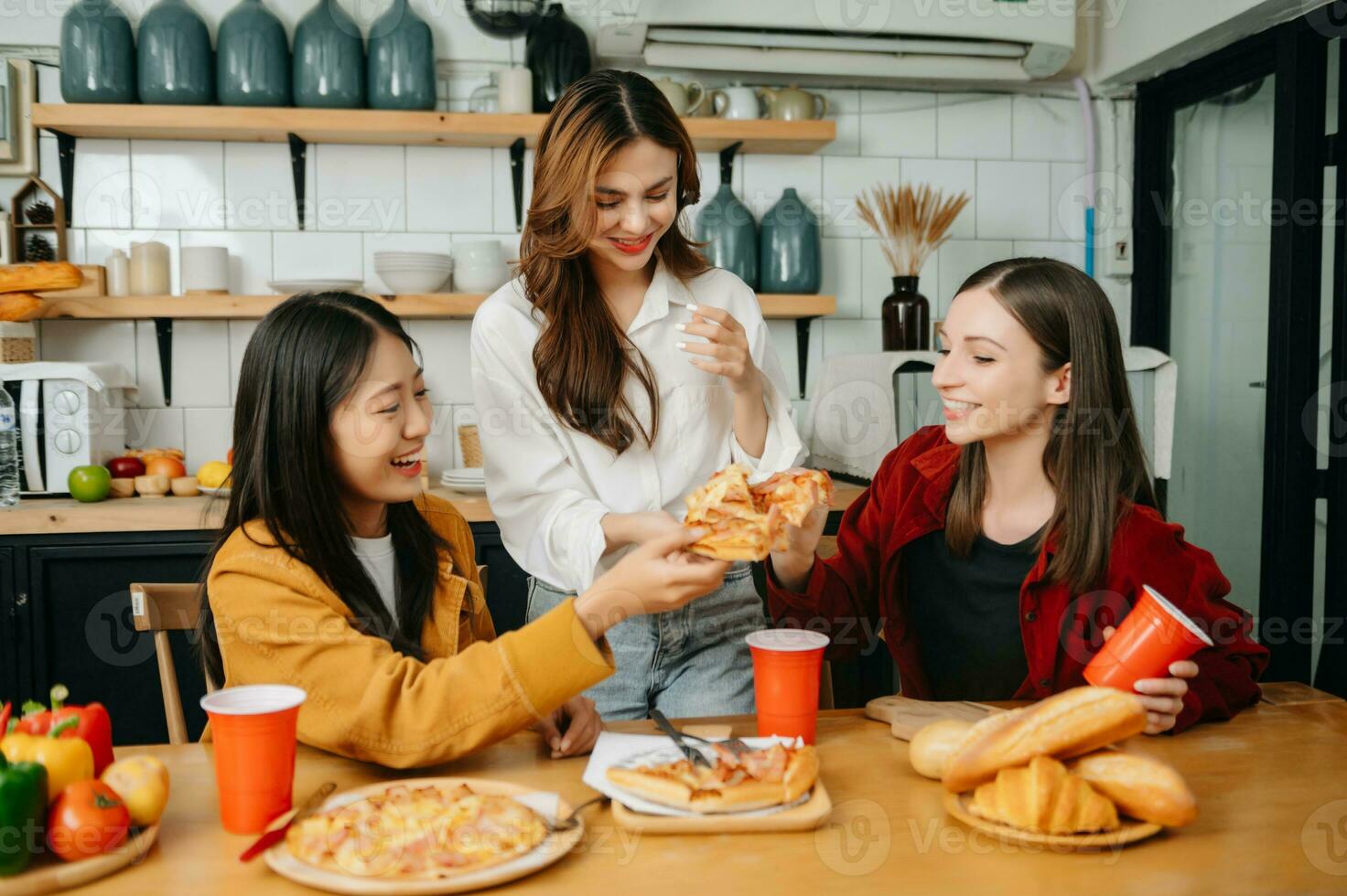 Group of friends making fun at home party.They sitting on desk in living room and eating pizza. happy photo