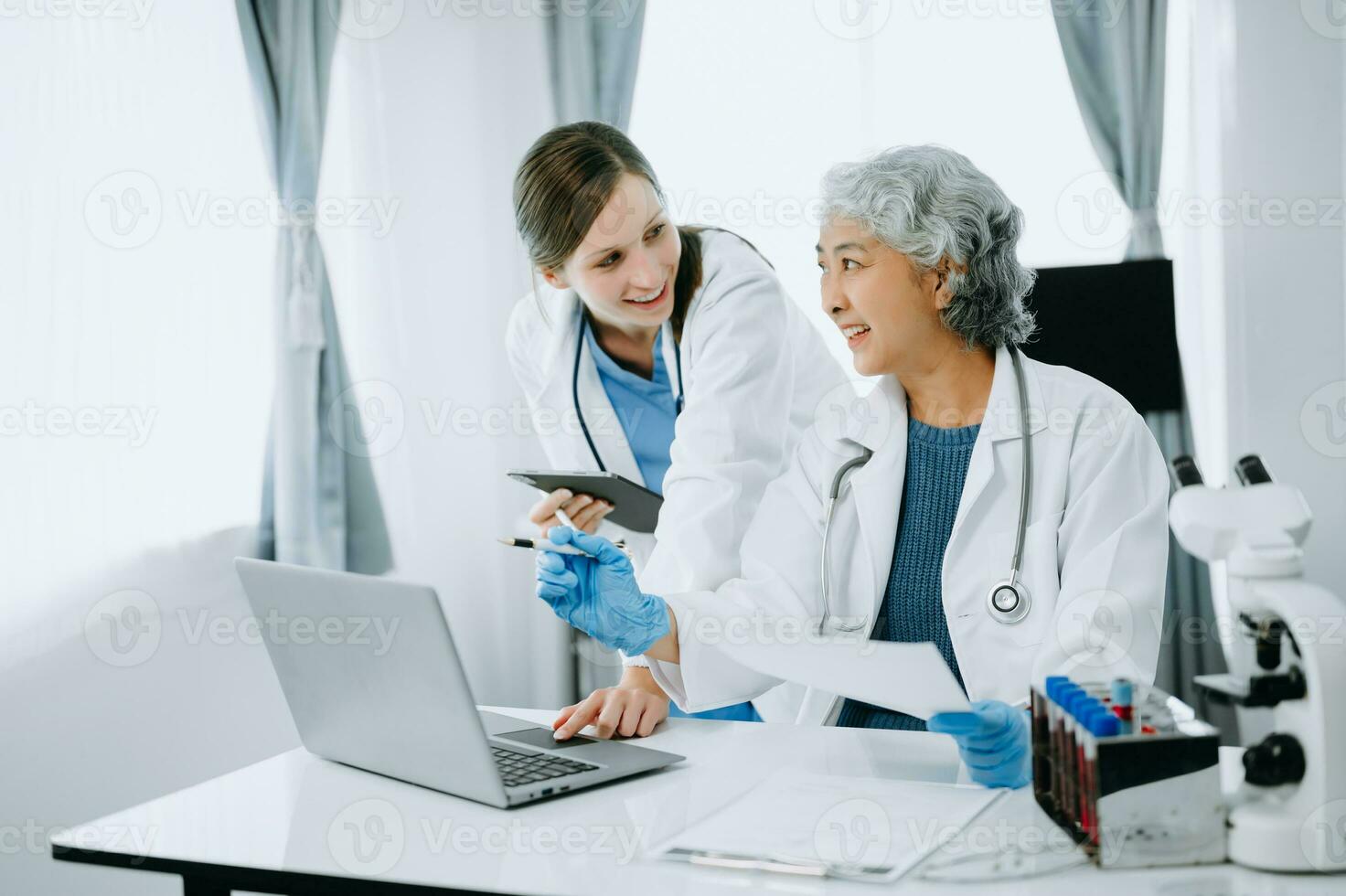 Medical team having a meeting with doctors in white lab coats and surgical scrubs seated at a table discussing a patients working online using computers in the medical industry photo