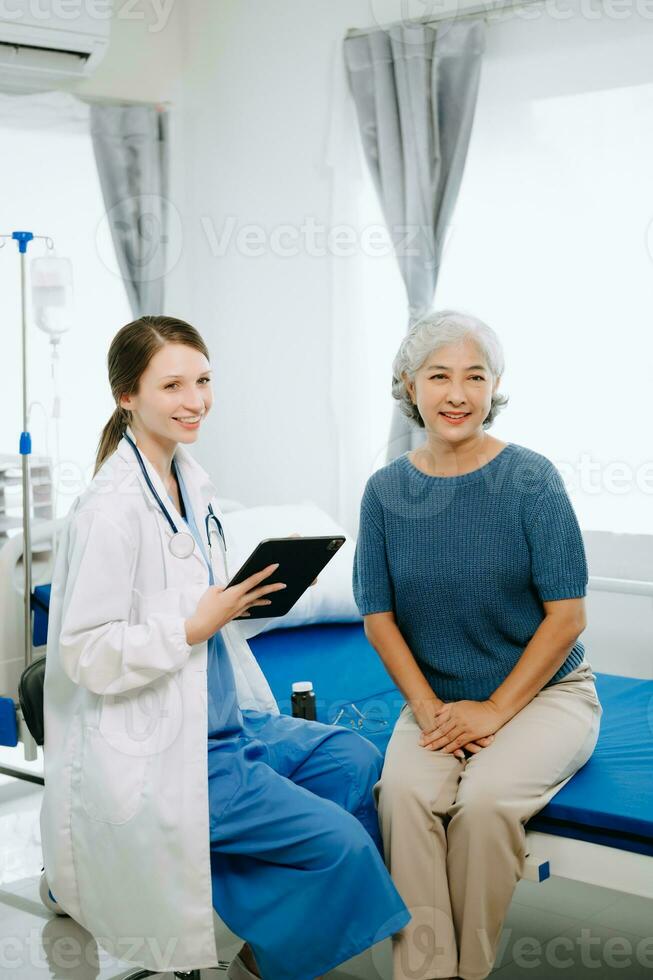 Friendly Female Head Nurse Making Rounds does Checkup on Patient Resting in Bed. She Checks tablet while Man Fully Recovering after Successful Surgery in hospital photo