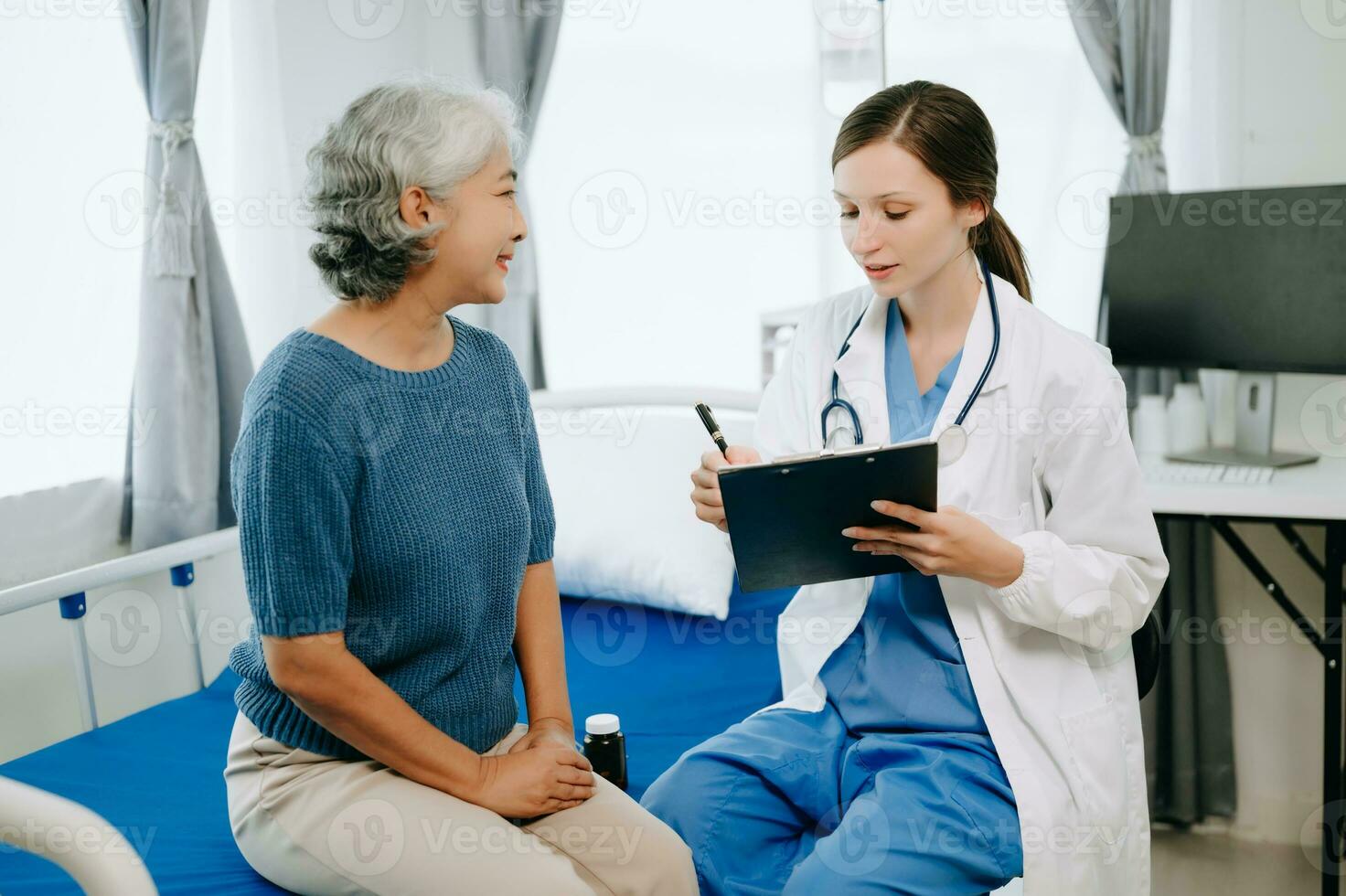 Friendly Female Head Nurse Making Rounds does Checkup on Patient Resting in Bed. She Checks tablet while Man Fully Recovering after Successful Surgery in hospital photo