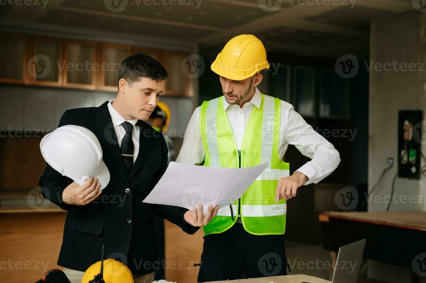 Contractor and architect looking at plan, tablet, laptop and talking about working on big project. Building in construction interior. photo