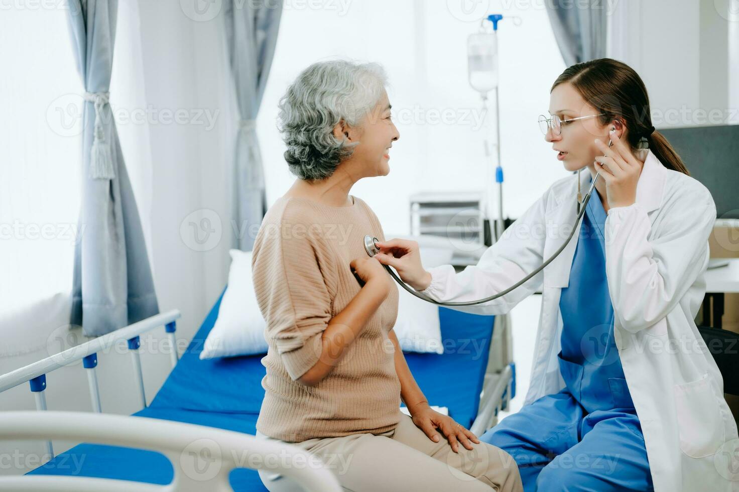 Friendly Female Head Nurse Making Rounds does Checkup on Patient Resting in Bed. She Checks tablet while Man Fully Recovering after Successful Surgery in hospital photo