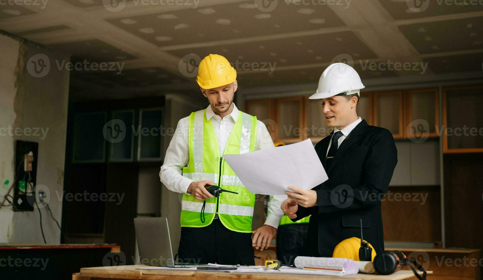 Contractor and architect looking at plan, tablet, laptop and talking about working on big project. Building in construction interior. photo