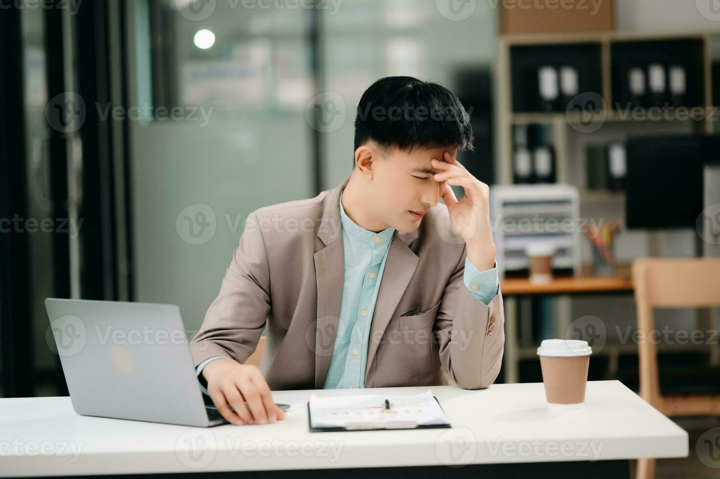 Frustrated young businessman working on a laptop computer sitting at his working place in office photo