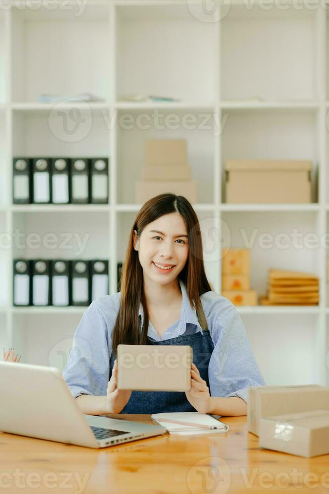 Asian young woman SME working using smartphone or tablet taking receive and checking online purchase shopping order photo