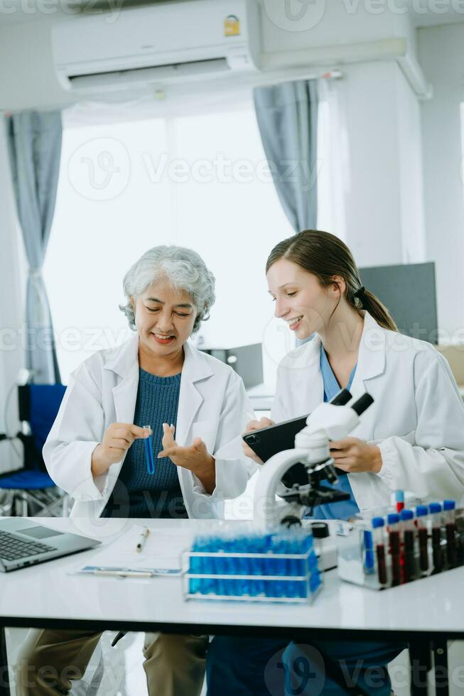 Two scientist or medical technician working, having a medical discuss meeting with an Asian senior female scientist supervisor in the laboratory with online reading, test samples and innovation photo