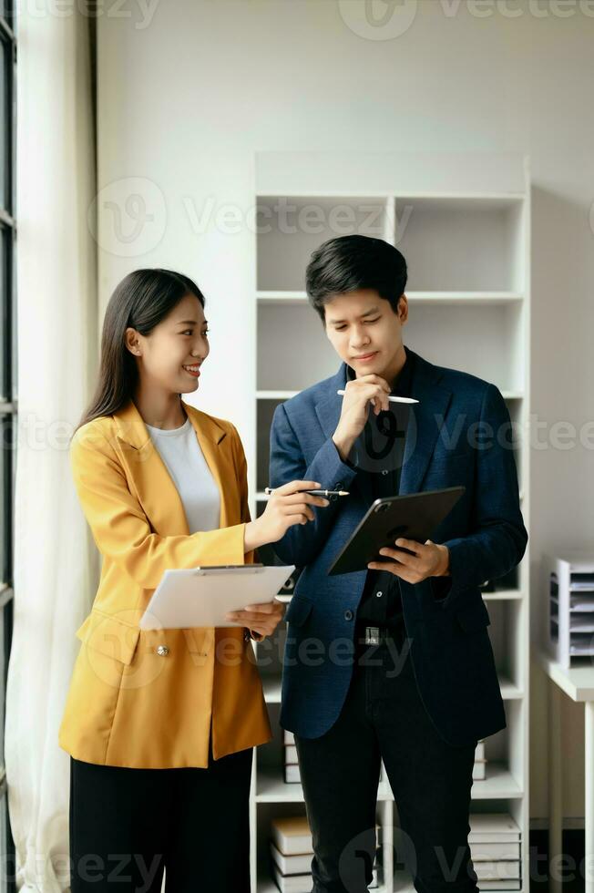 Two Asian business woman and man  discuss investment project working and planning strategy with tablet laptop computer in office. photo
