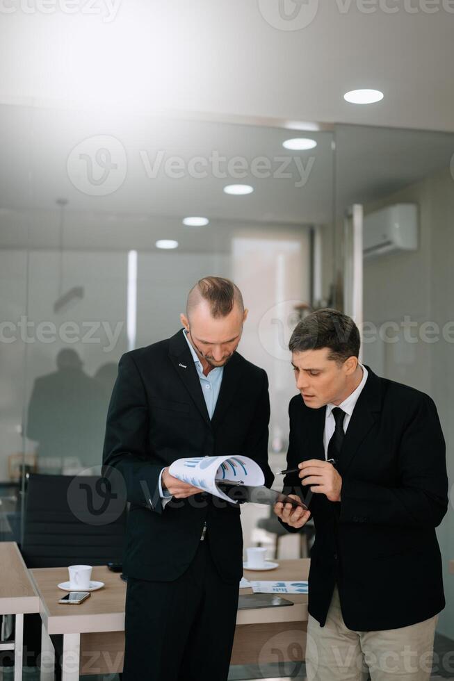 Male discussing new project with male colleague. Mature man talking with young man in office. photo
