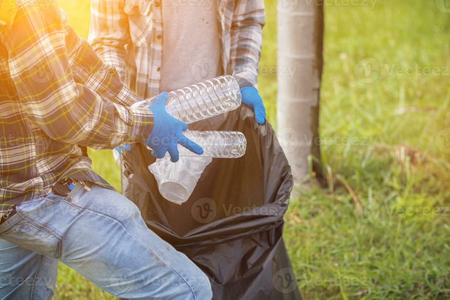 Two man employees use black garbage bags to collect plastic bottles and recyclable waste from the lawn and sidewalks for recycling. Concept of sorting plastic waste for recycling photo
