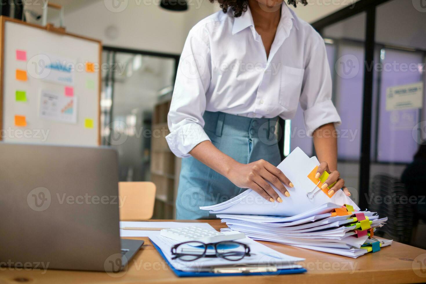 secretary searches through stacked documents on desk in office to find lease within stacked documents just before meeting. concept difficulty in finding hire purchase contract from stacked documents photo