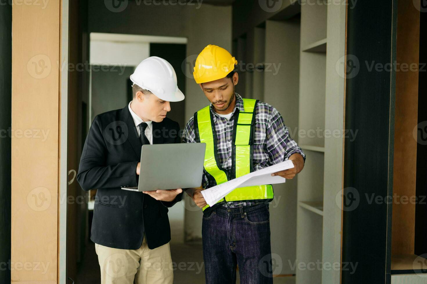 Contractor and architect looking at plan, tablet, laptop and talking about working on big project. Building in construction process photo