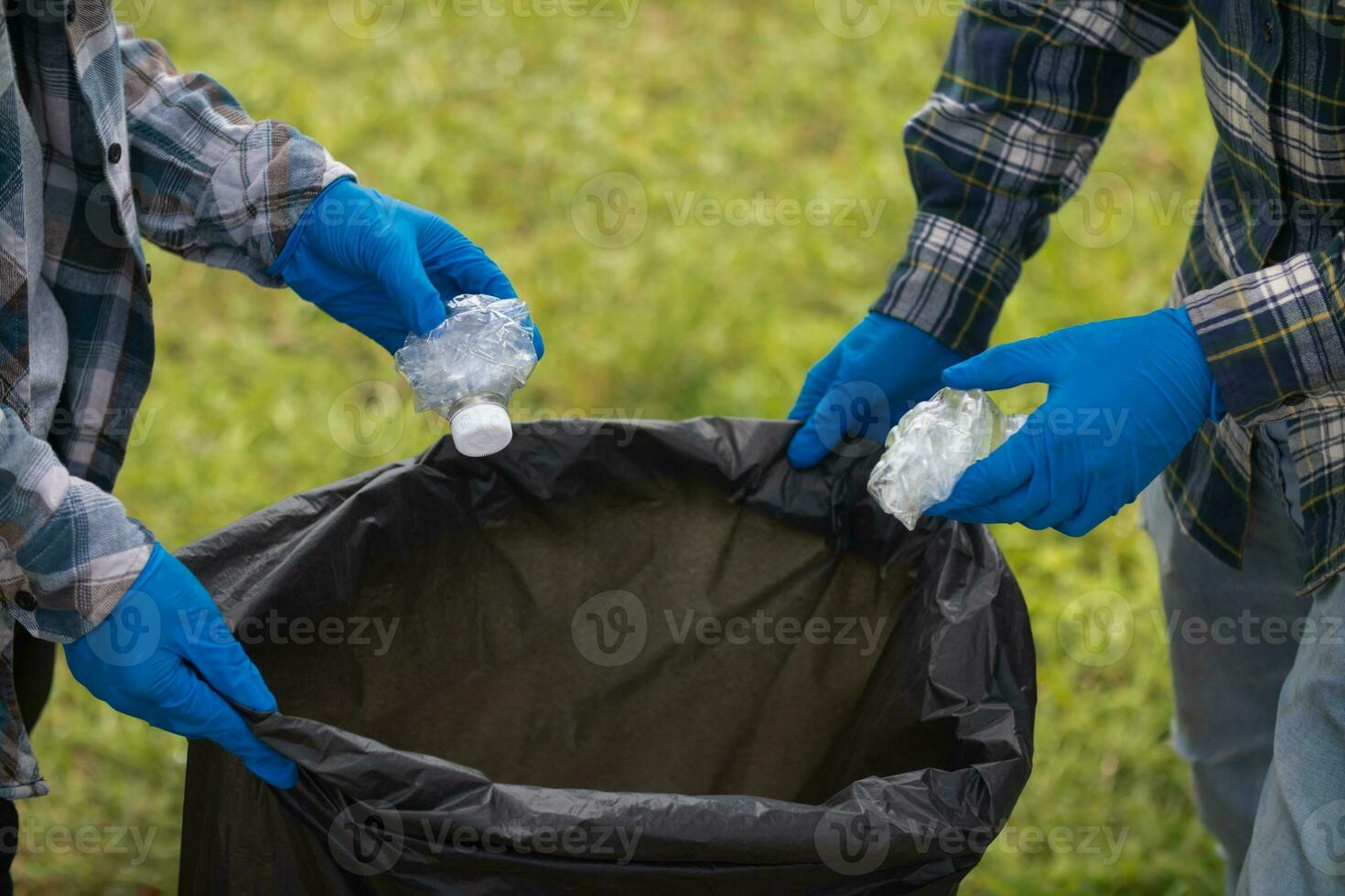 Two man employees use black garbage bags to collect plastic bottles and recyclable waste from the lawn and sidewalks for recycling. Concept of sorting plastic waste for recycling photo