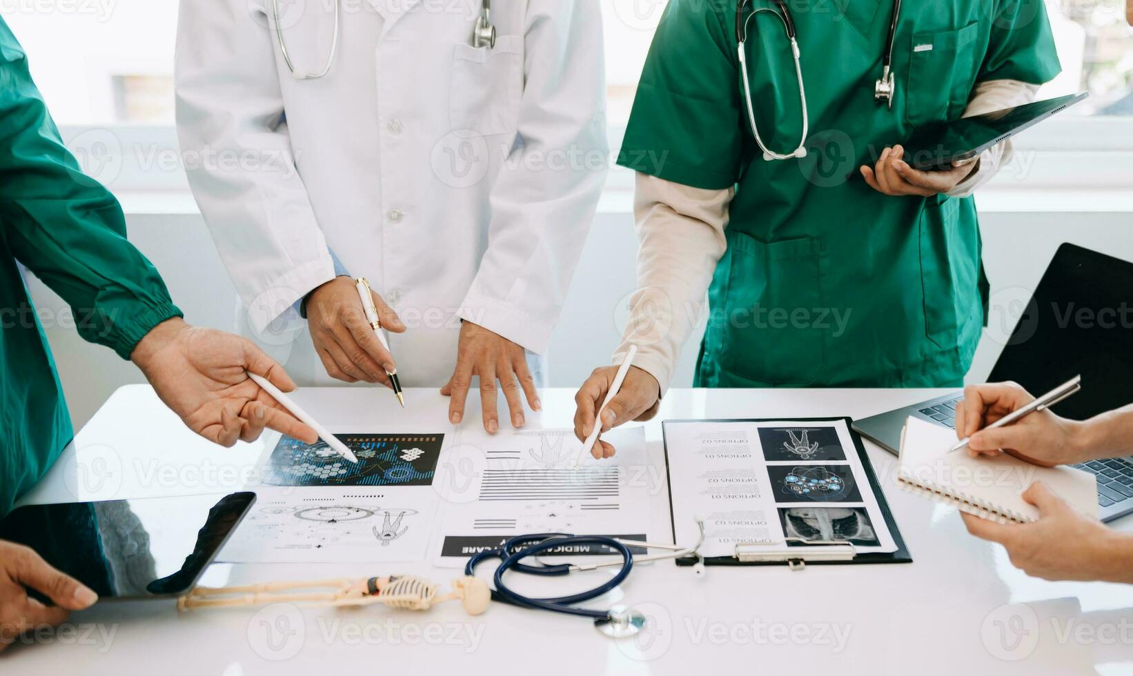Medical team having a meeting with doctors in white lab coats and surgical scrubs seated at a desk discussing a patients working online using computers in the medical industry photo