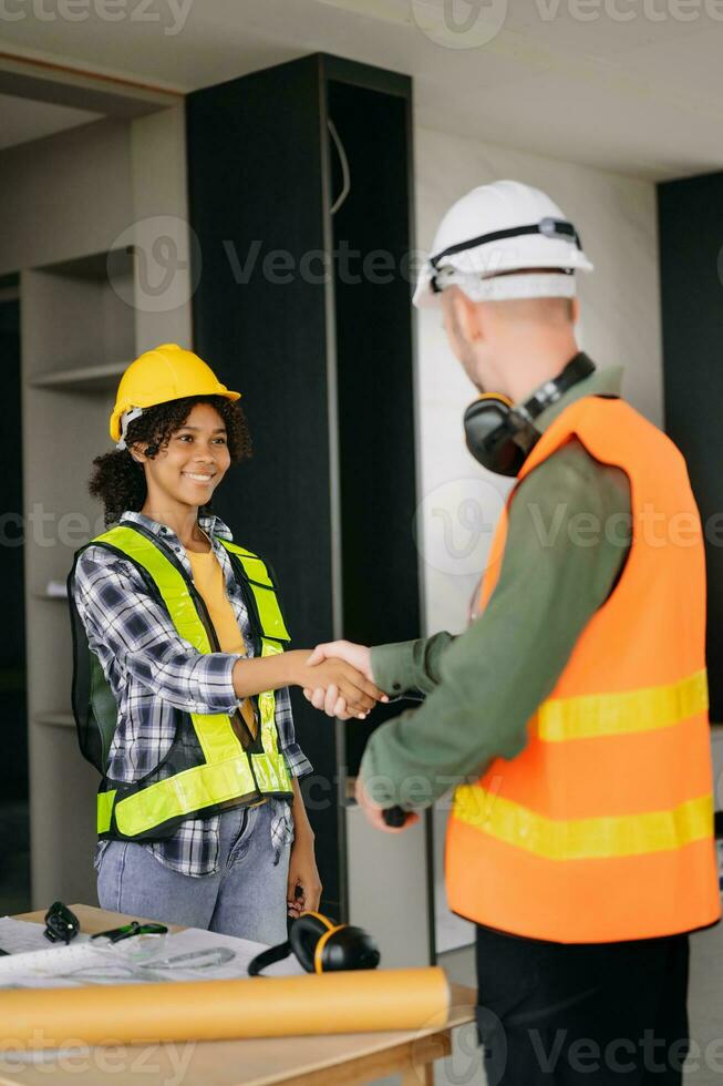 Construction team shake hands greeting start new project plan behind yellow helmet on desk in office center to consults about their building project. photo