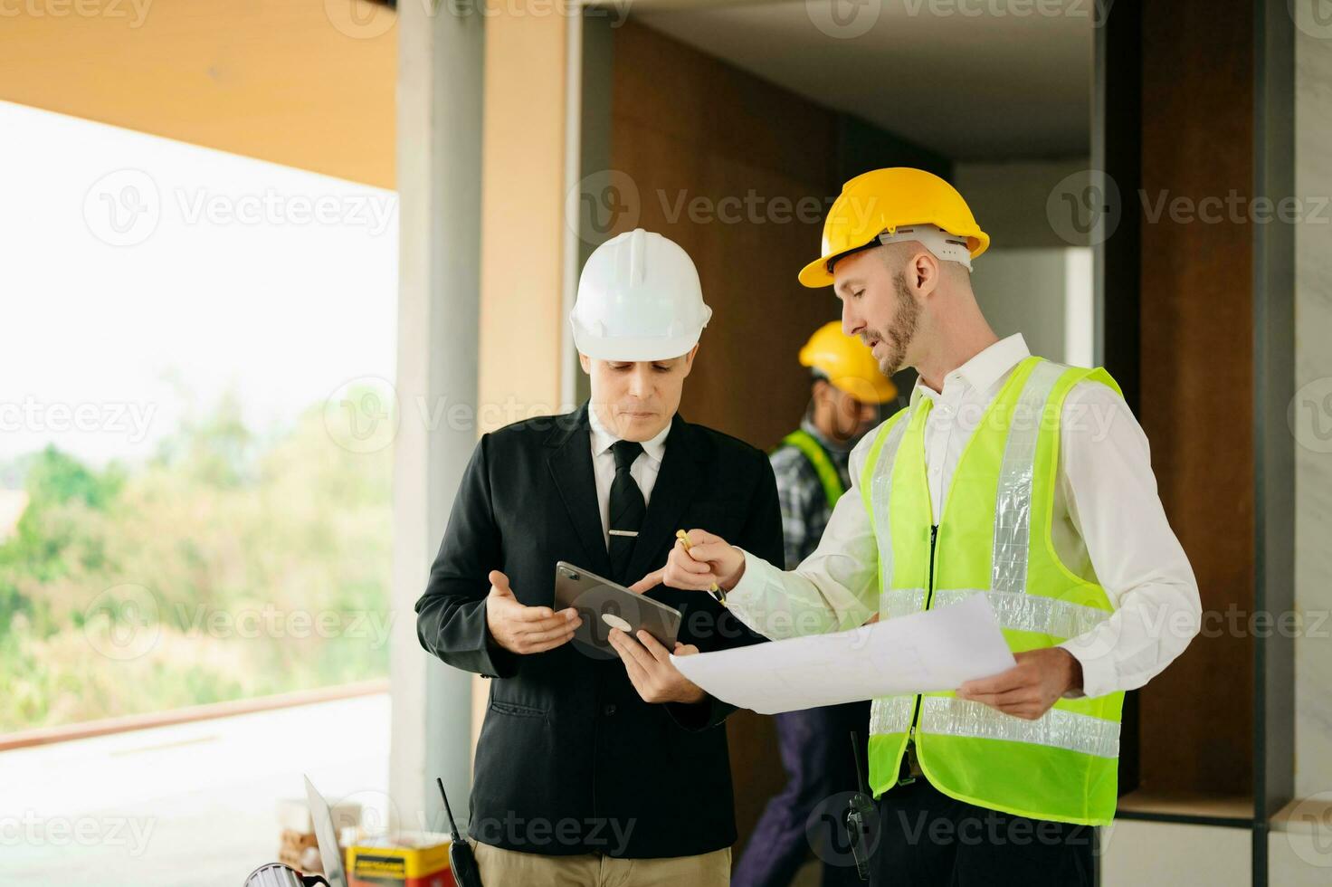 Contractor and architect looking at plan, tablet, laptop and talking about working on big project. Building in construction process photo