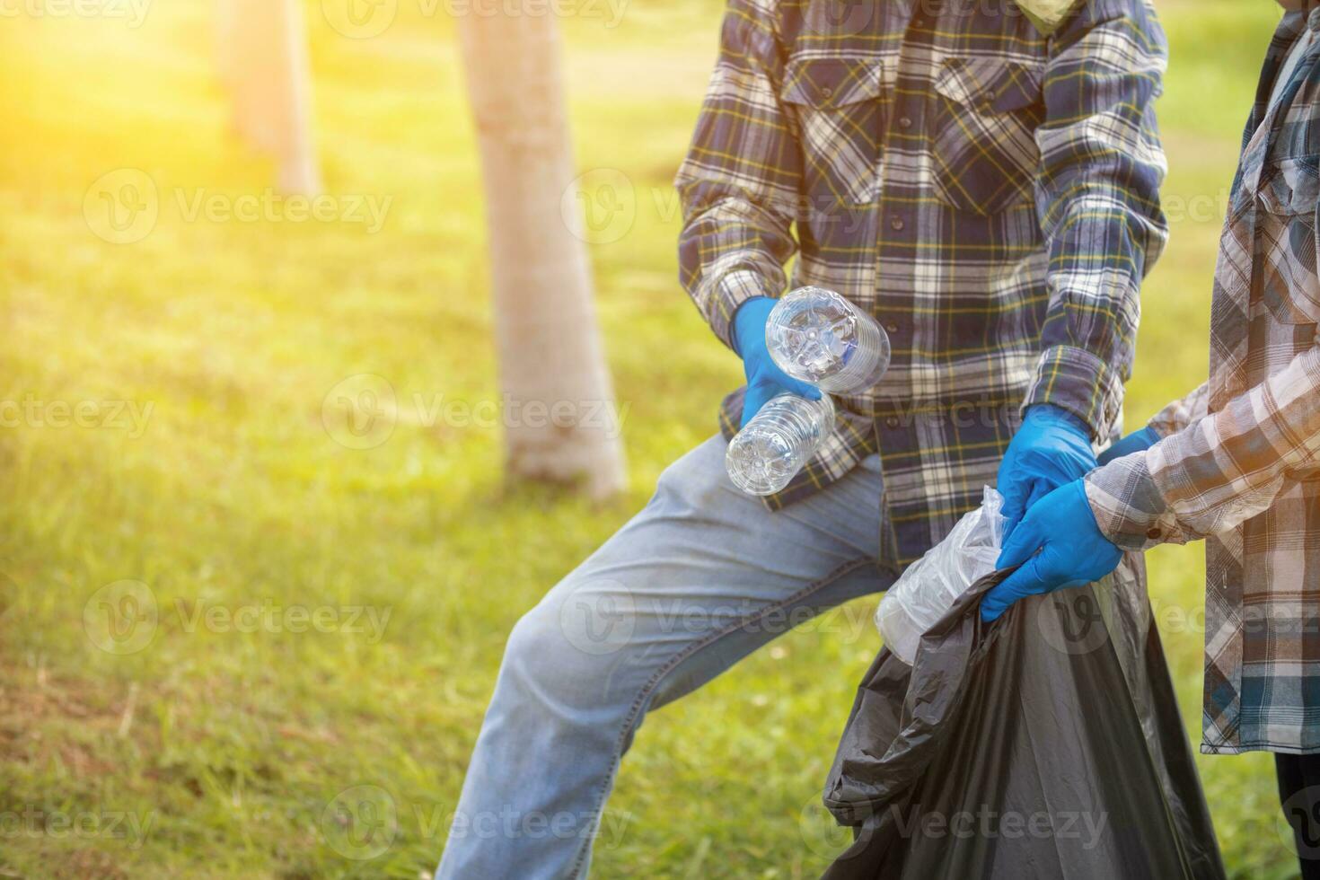 men collect plastic bottles on lawns and walkways in park and put them in bags to help keep them clean They can also collect plastic bottles for recycling. reducing environmental problems by recycling photo