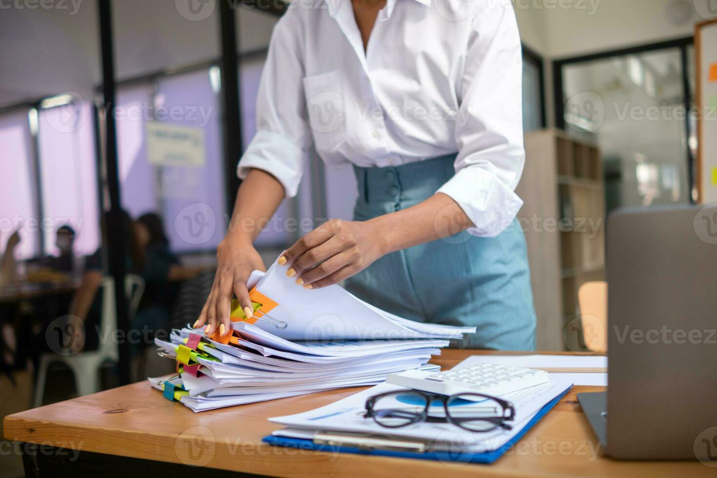 secretary searches through stacked paperwork on desk in office to find lease within stacked paperwork just before meeting. concept difficulty in finding hire purchase contract from stacked paperwork photo