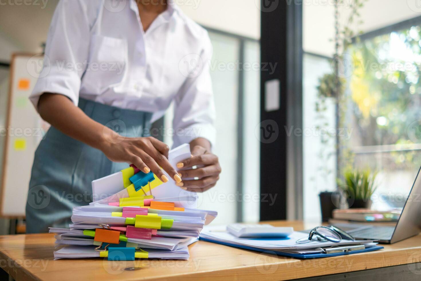 secretary searches through stacked documents on desk in office to find lease within stacked documents just before meeting. concept difficulty in finding hire purchase contract from stacked documents photo