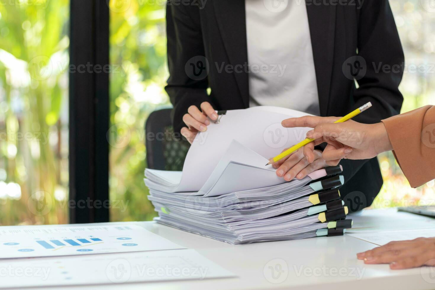 secretary searches through stacked paperwork on desk in office to find lease within stacked paperwork just before meeting. concept difficulty in finding hire purchase contract from stacked paperwork photo