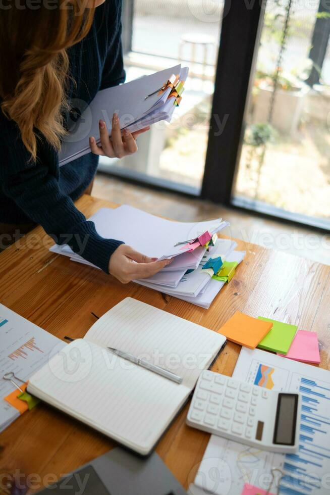 secretary searches through stacked documents on desk in office to find lease within stacked documents just before meeting. concept difficulty in finding hire purchase contract from stacked documents photo
