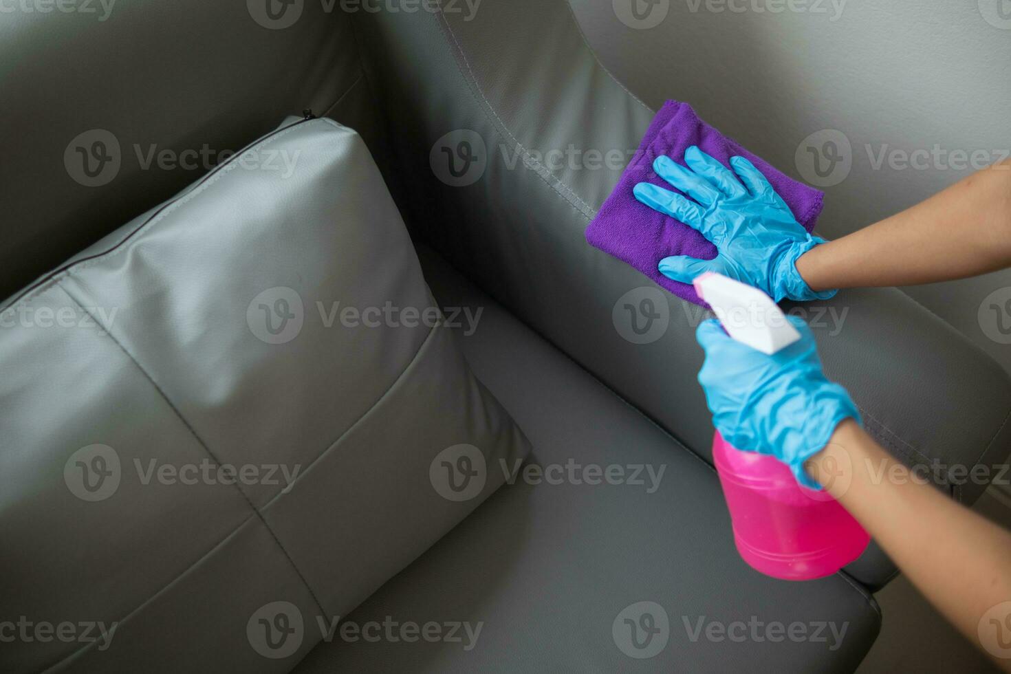 Cleaning staff is wiping cloth with cleaner and disinfectant on the surface of sofa to make the sofa clean with cleaning products and free from germs clinging to surface of the sofa in living room. photo