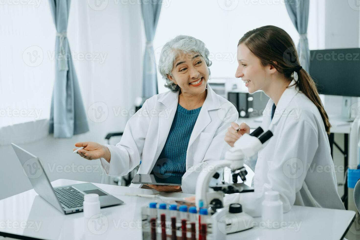 Two scientist or medical technician working, having a medical discuss meeting with an Asian senior female scientist supervisor in the laboratory with online reading, test samples and innovation photo