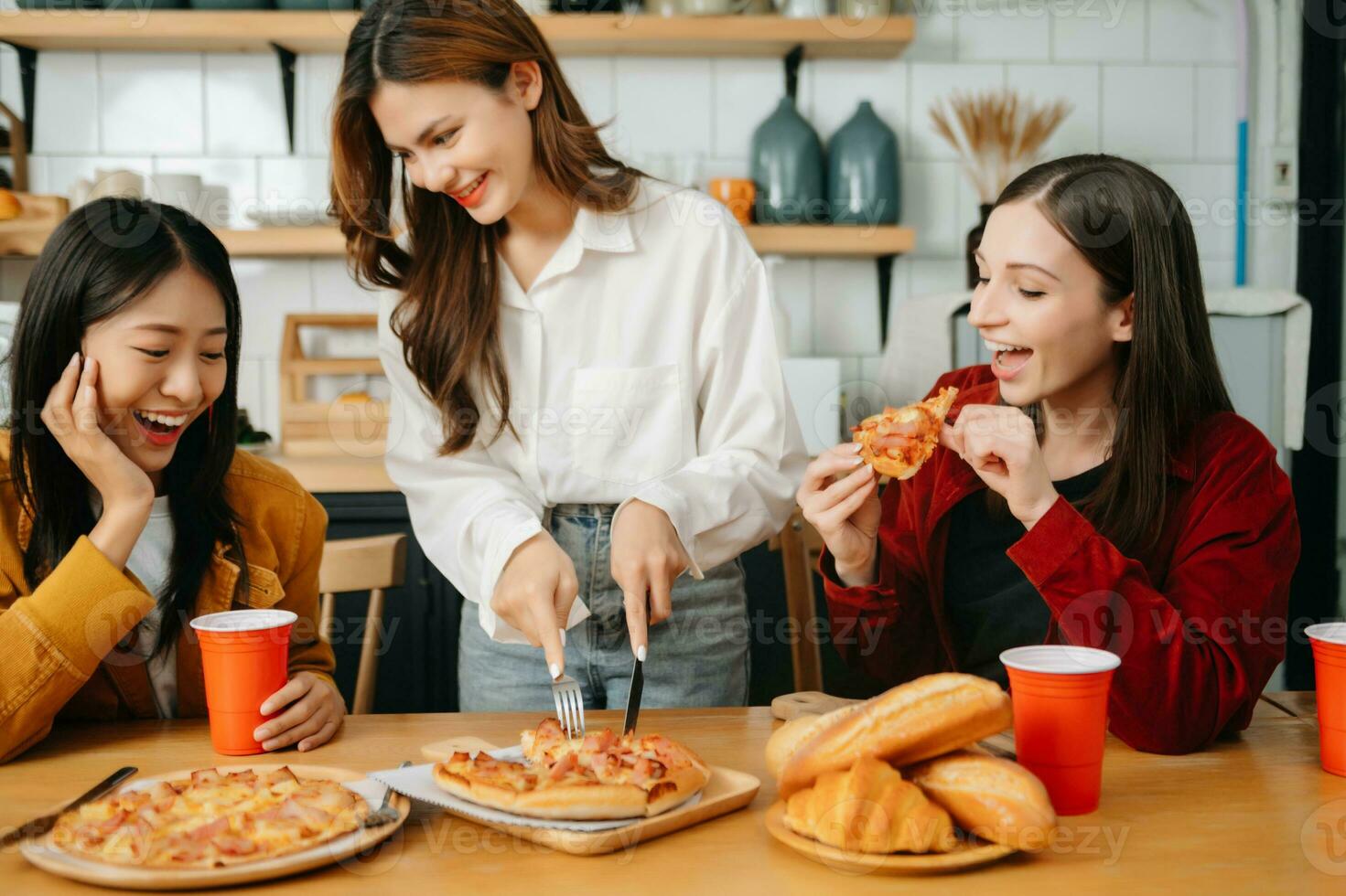 Group of friends making fun at home party.They sitting on desk in living room and eating pizza. happy photo