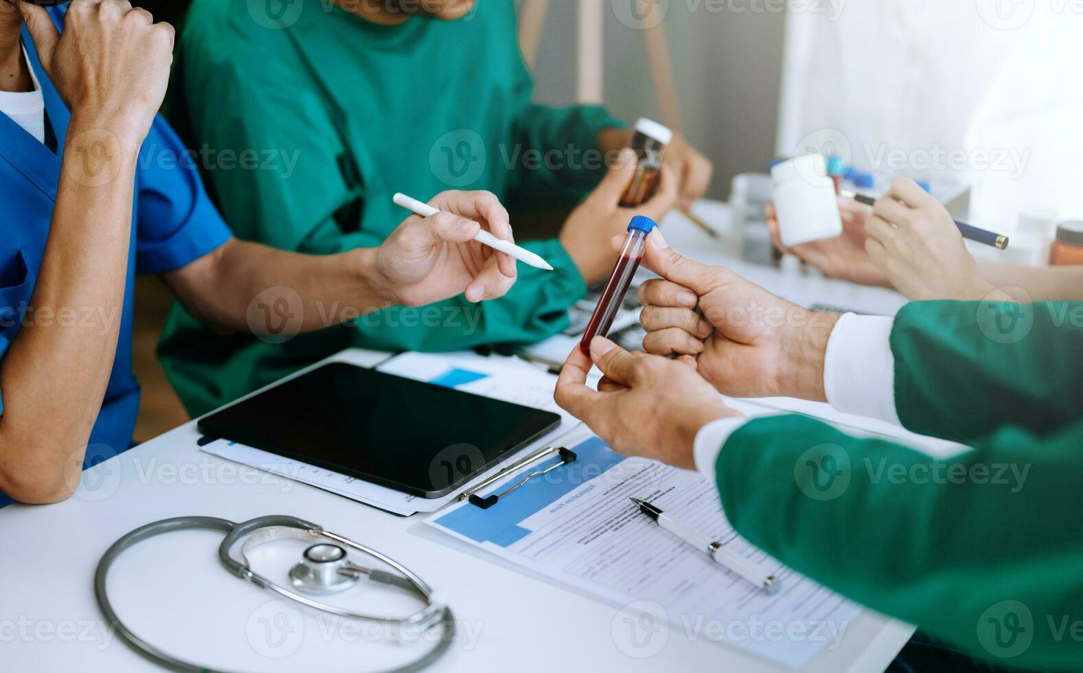 Medical team having a meeting with doctors in white lab coats and surgical scrubs seated at a table discussing a patients working online using computers photo