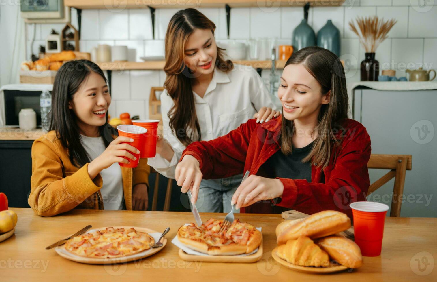 Group of friends making fun at home party.They sitting on desk in living room and eating pizza. photo