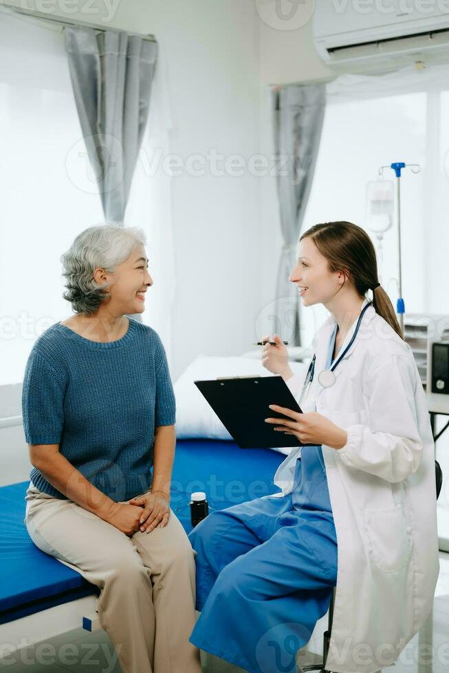 Friendly Female Head Nurse Making Rounds does Checkup on Patient Resting in Bed. She Checks tablet while Man Fully Recovering after Successful Surgery in hospital photo