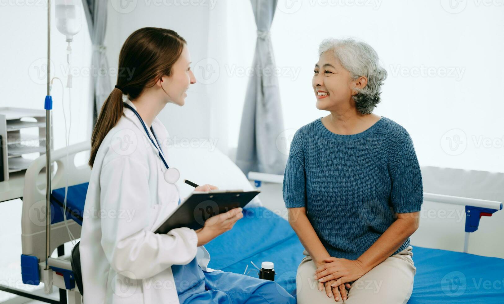 Friendly Female Head Nurse Making Rounds does Checkup on Patient Resting in Bed. She Checks tablet while Man Fully Recovering after Successful Surgery in hospital photo