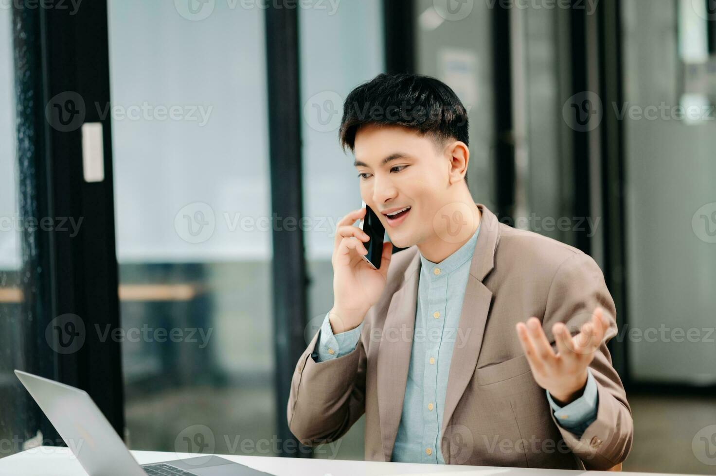 Business asian man Talking on the phone and using a laptop with a smile while sitting at modern office photo