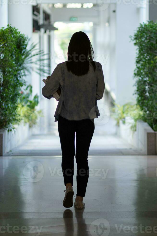 female international school student dressed in jeans walked inside school building on corridor in front of classroom alone. back of female student who was walking alone in corridor of school building. photo