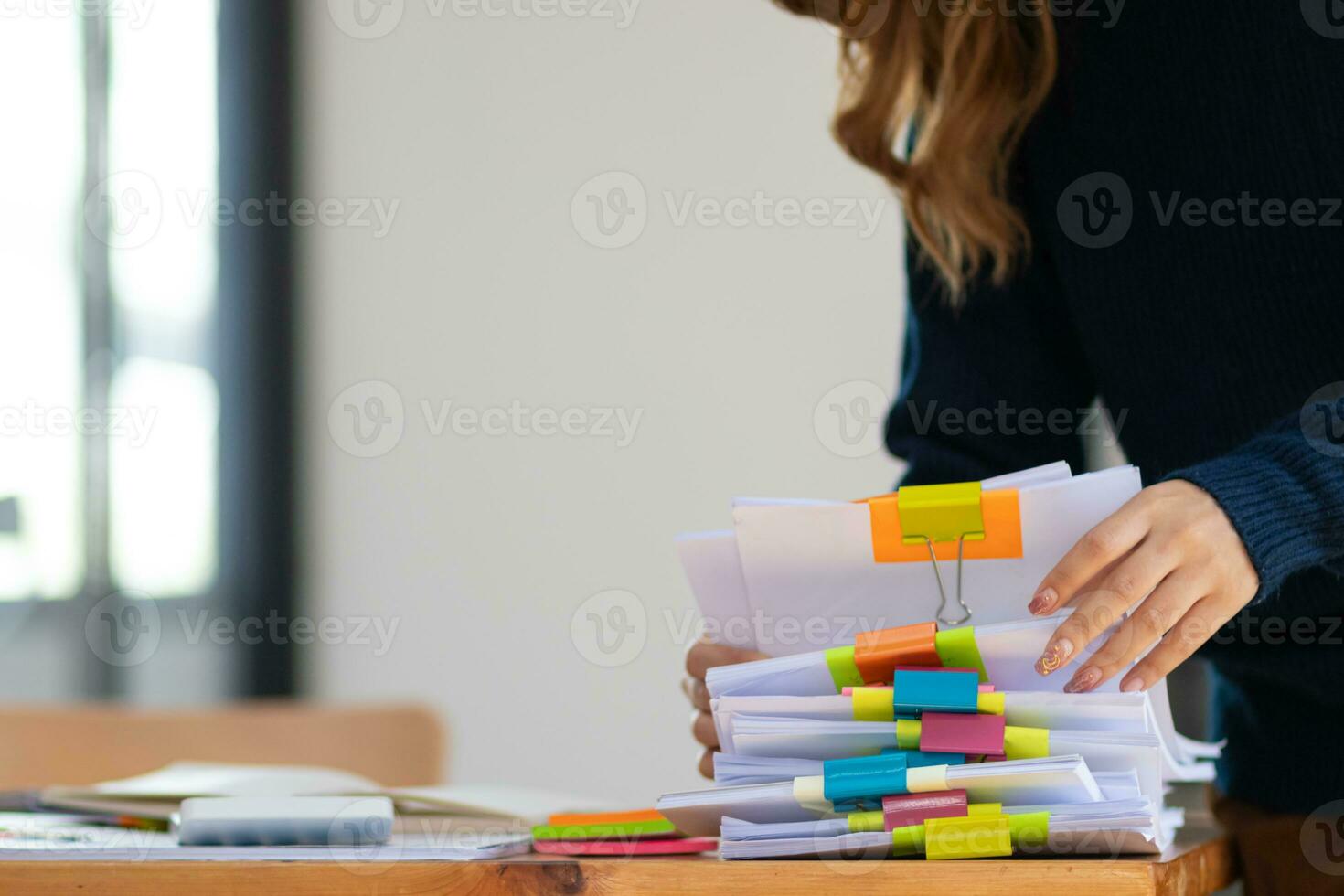 secretary searches through stacked documents on desk in office to find lease within stacked documents just before meeting. concept difficulty in finding hire purchase contract from stacked documents photo
