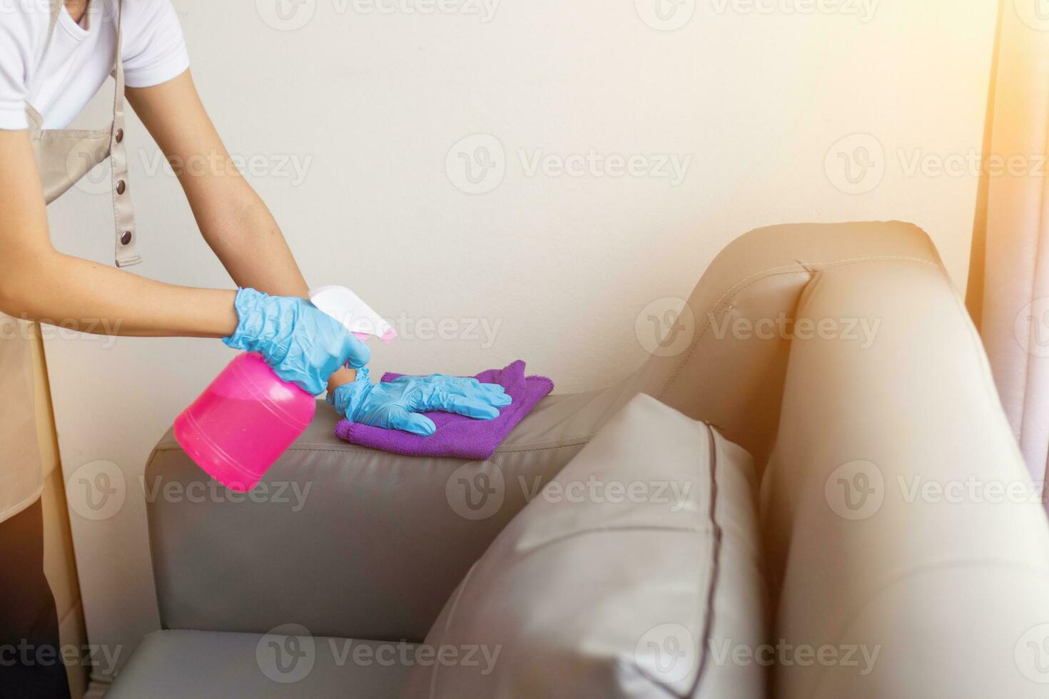 Cleaning staff is wiping cloth with cleaner and disinfectant on the surface of sofa to make the sofa clean with cleaning products and free from germs clinging to surface of the sofa in living room. photo