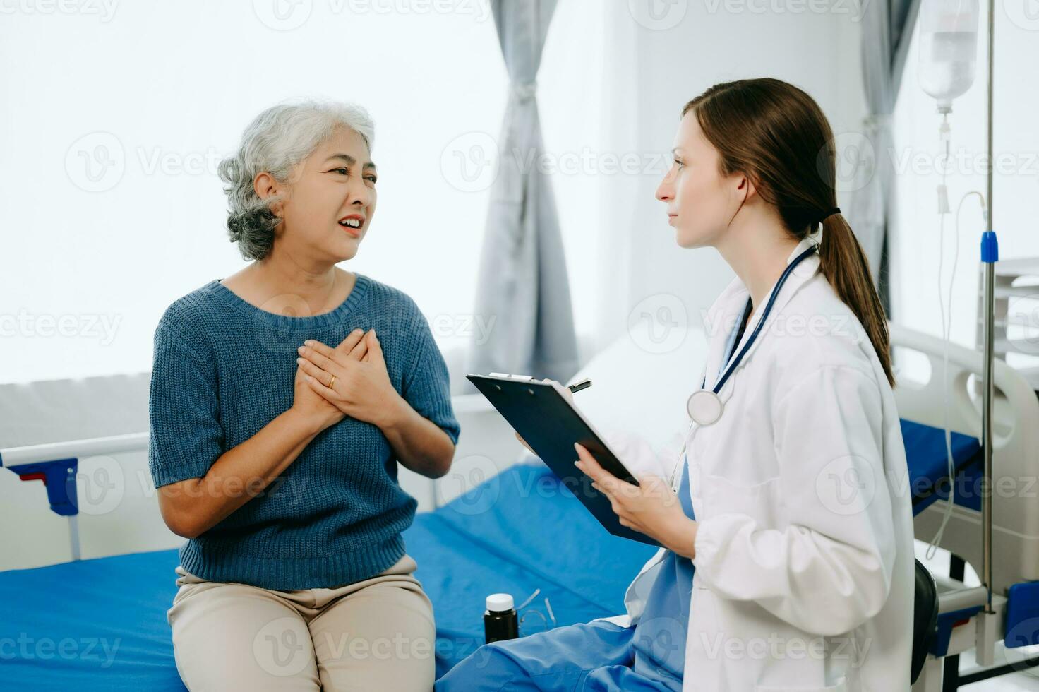 Friendly Female Head Nurse Making Rounds does Checkup on Patient Resting in Bed. She Checks tablet while Man Fully Recovering after Successful Surgery in hospital photo