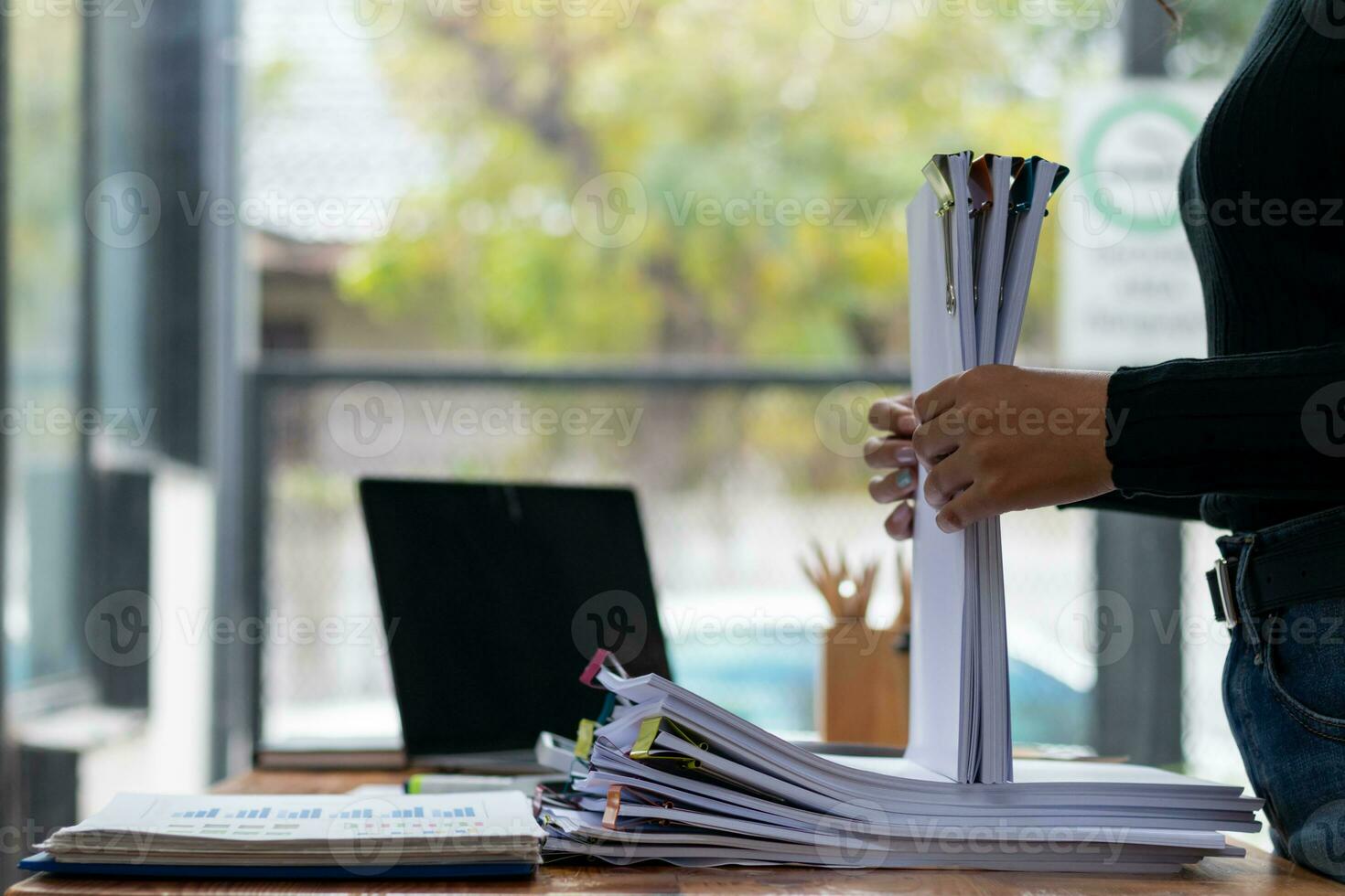 secretary searches through stacked documents on desk in office to find lease within stacked documents just before meeting. concept difficulty in finding hire purchase contract from stacked documents photo