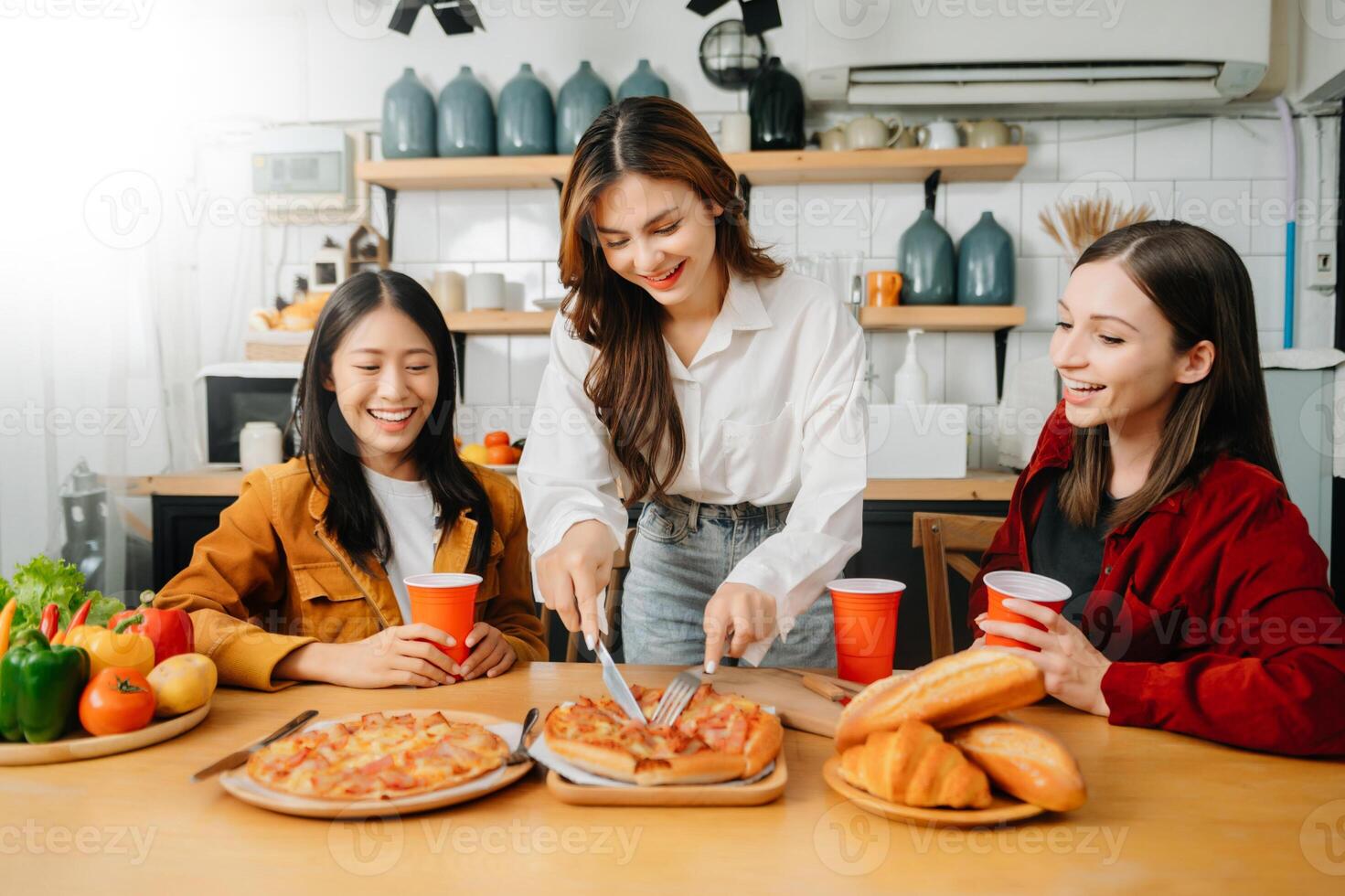 Group of friends making fun at home party.They sitting on desk in living room and eating pizza. photo