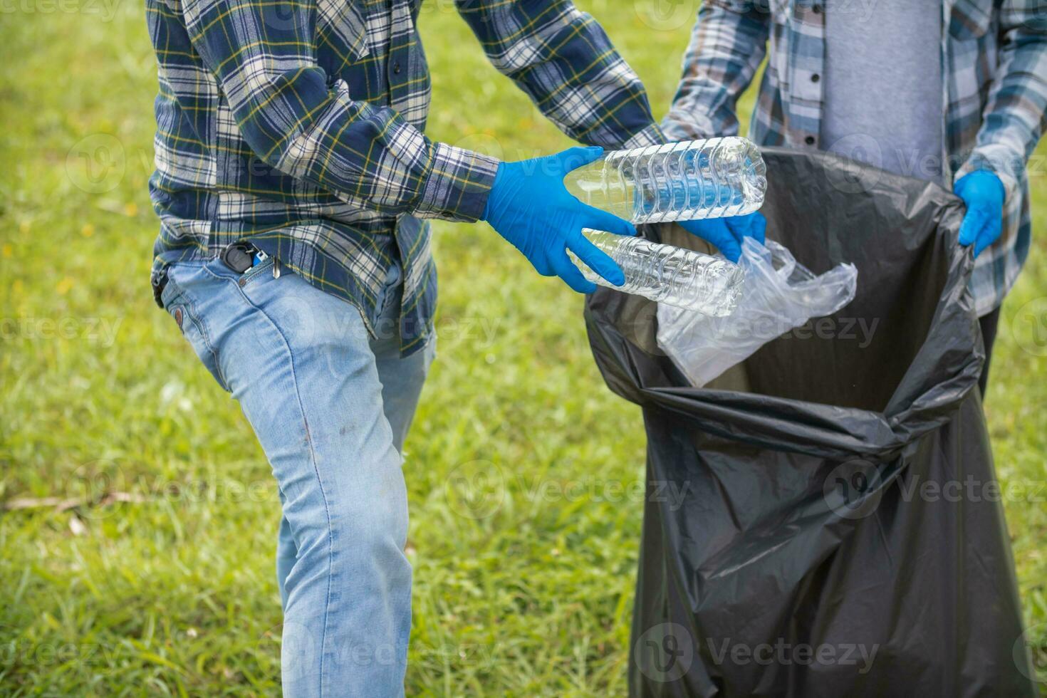 Two man employees use black garbage bags to collect plastic bottles and recyclable waste from the lawn and sidewalks for recycling. Concept of sorting plastic waste for recycling photo