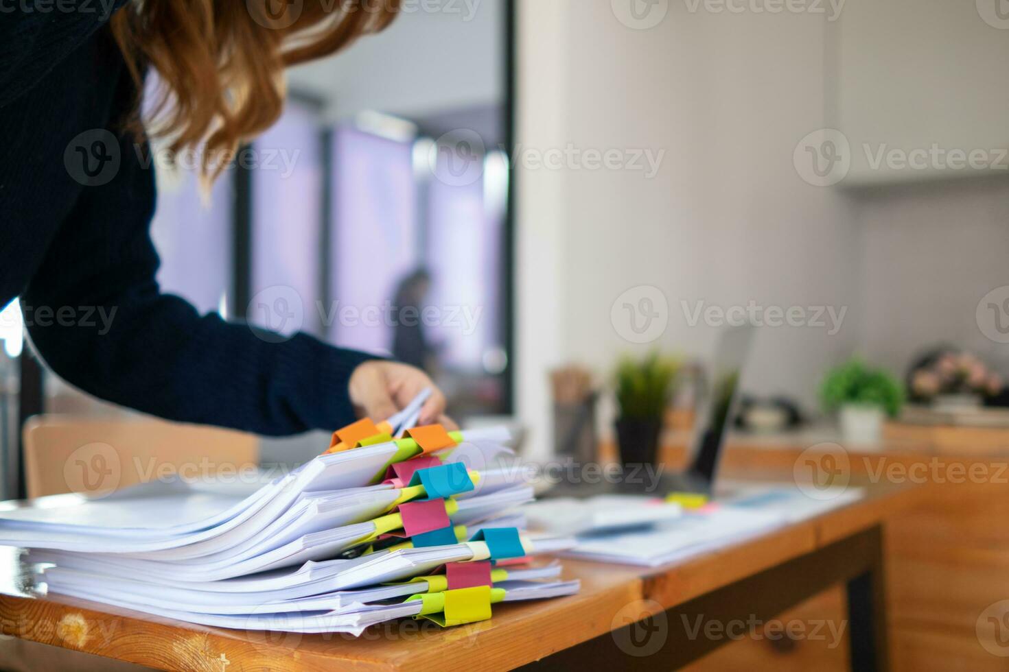 secretary searches through stacked paperwork on desk in office to find lease within stacked paperwork just before meeting. concept difficulty in finding hire purchase contract from stacked paperwork photo