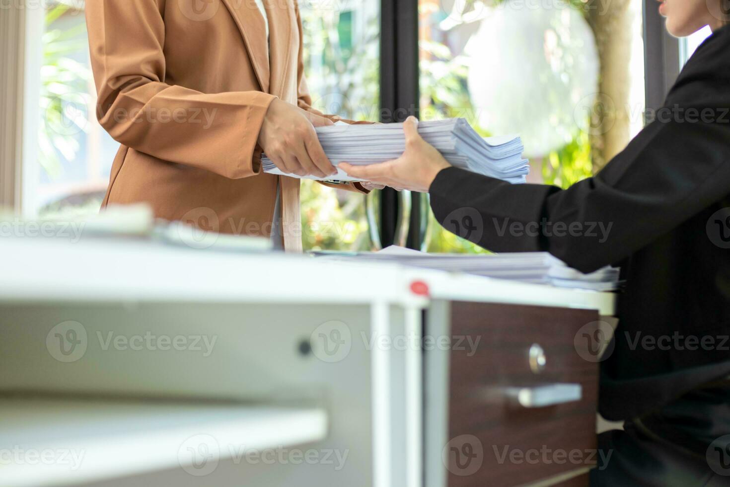secretary searches through stacked paperwork on desk in office to find lease within stacked paperwork just before meeting. concept difficulty in finding hire purchase contract from stacked paperwork photo