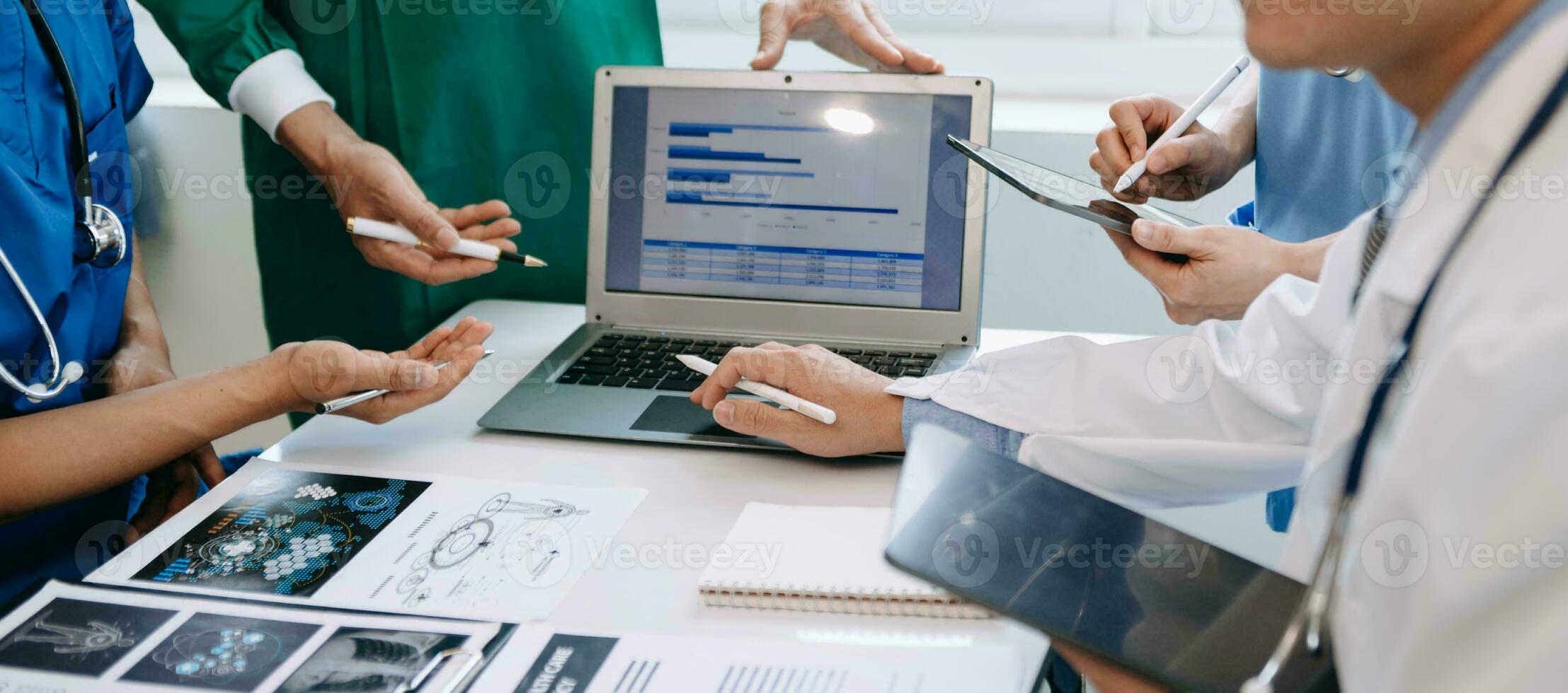 Medical team having a meeting with doctors in white lab coats and surgical scrubs seated at a table discussing a patients working online using computers in medical industry photo