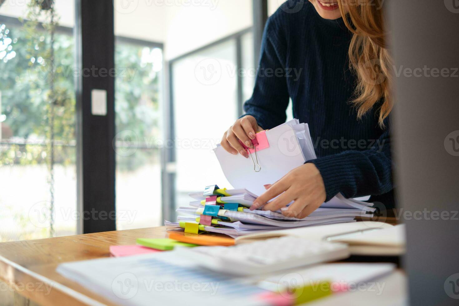 secretary searches through stacked documents on desk in office to find lease within stacked documents just before meeting. concept difficulty in finding hire purchase contract from stacked documents photo