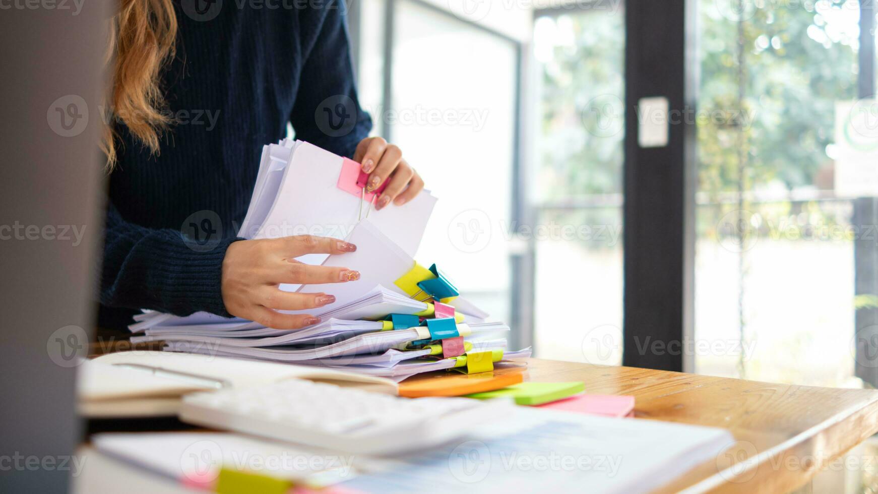 secretary searches through stacked paperwork on desk in office to find lease within stacked paperwork just before meeting. concept difficulty in finding hire purchase contract from stacked paperwork photo