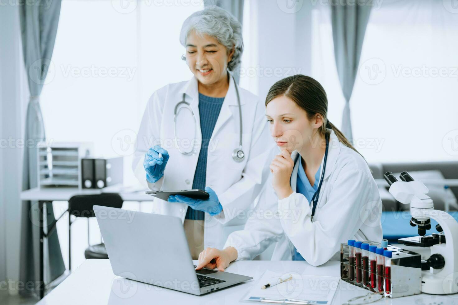 Medical team having a meeting with doctors in white lab coats and surgical scrubs seated at a table discussing a patients working online using computers in the medical industry photo