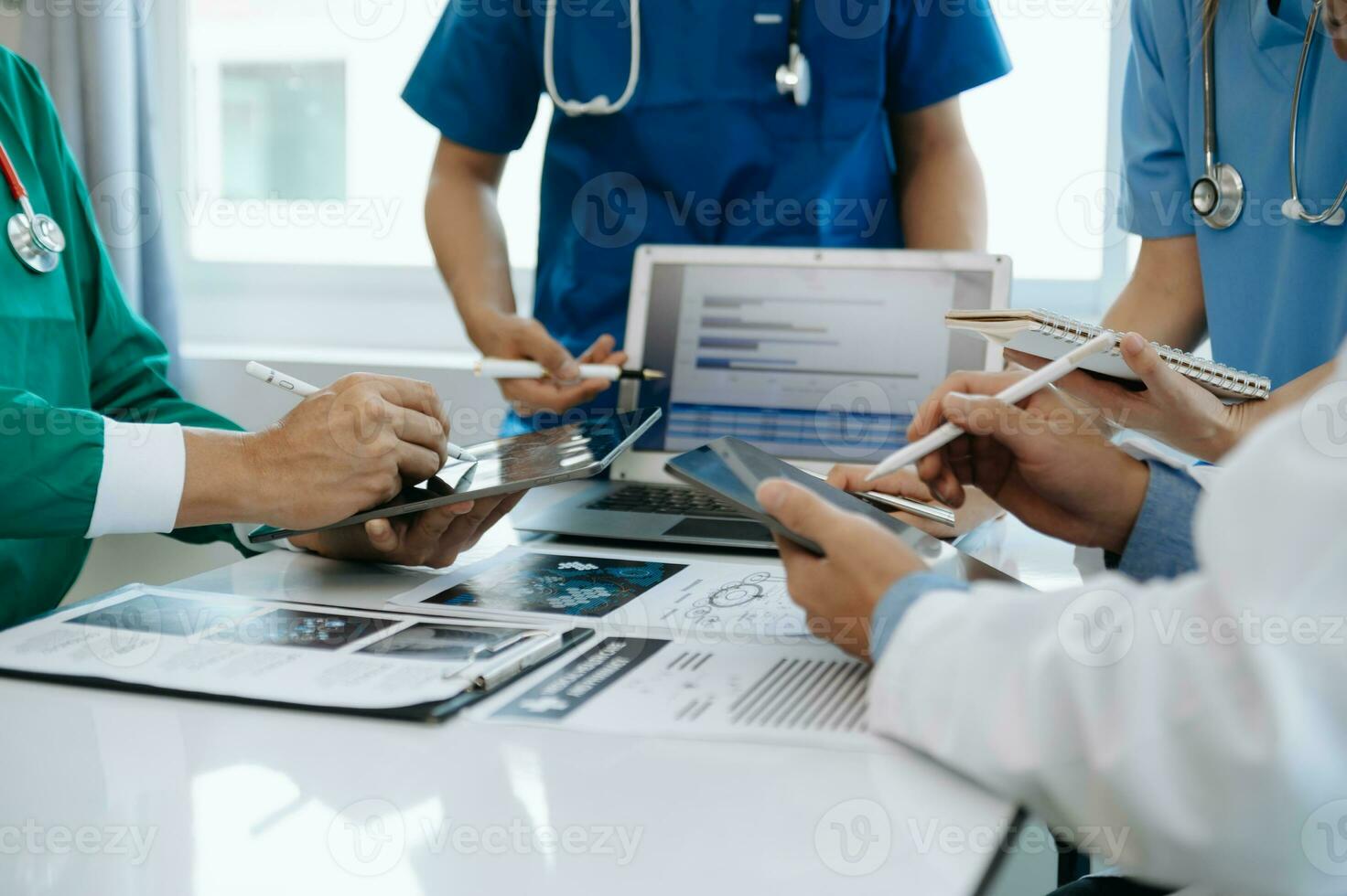 Medical team having a meeting with doctors in white lab coats and surgical scrubs seated at a table discussing a patients working online using computers in the medical industry photo